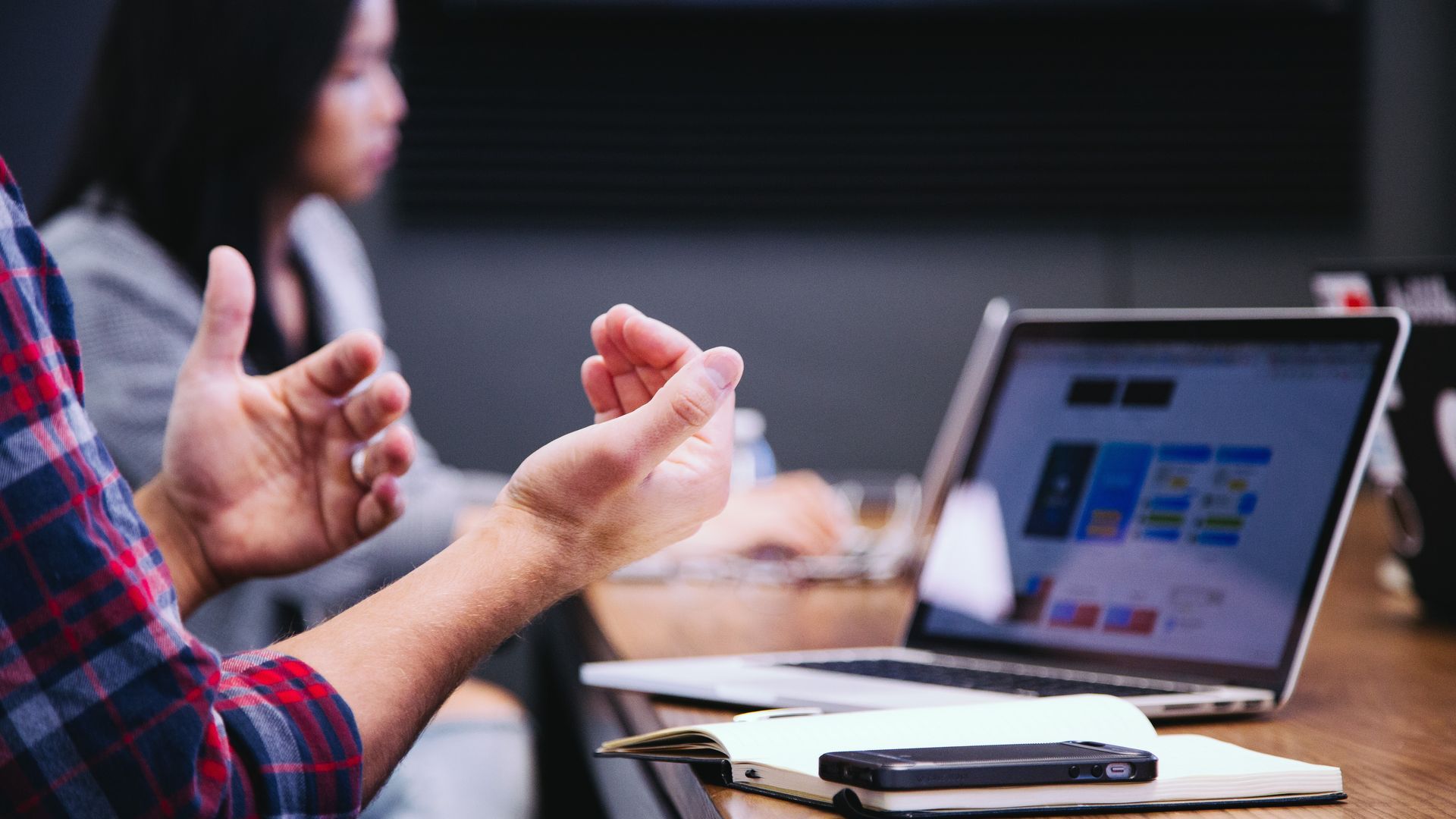 two people sitting at a conference table, one person's hands gesturing in front of an open laptop