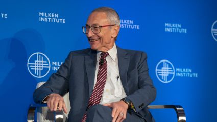 A man in business attire sitting on a stage
